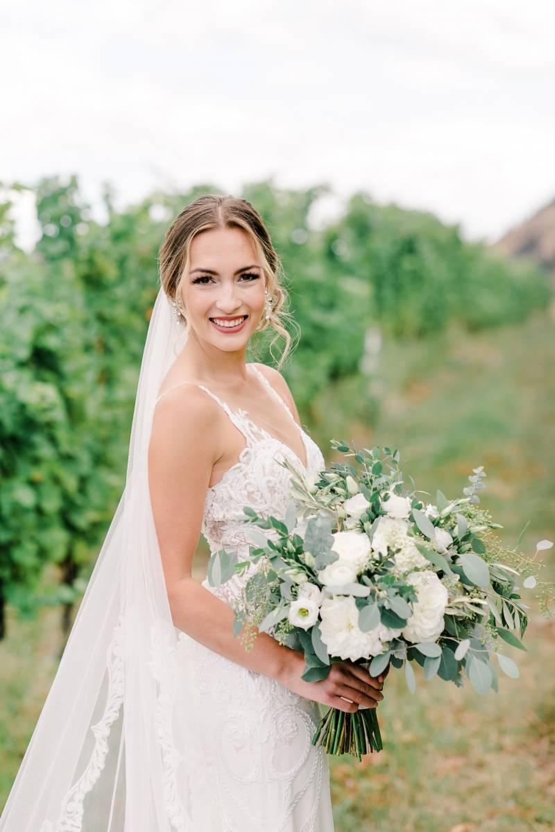 Bride holding white bouquet smiling in green peach field 
