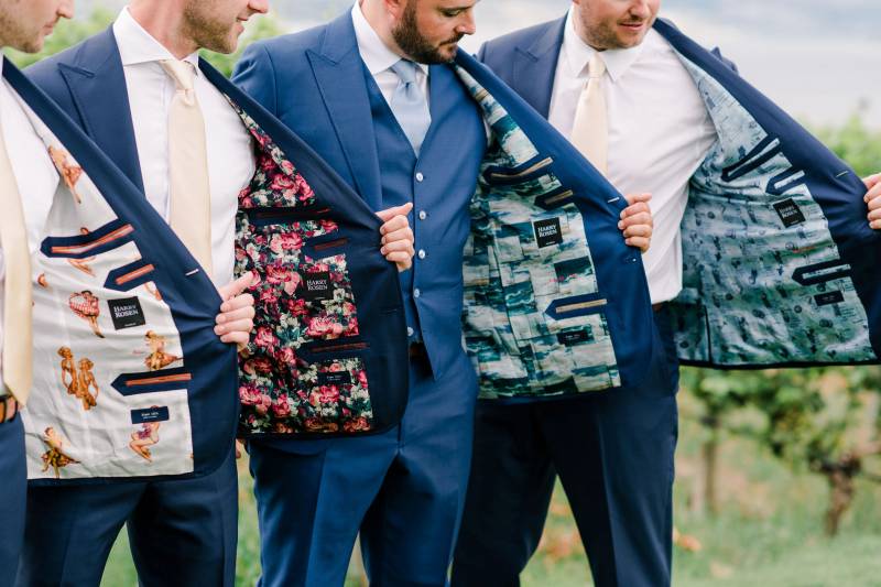 Groom and groomsmen hold open suit jackets with decorative linings 