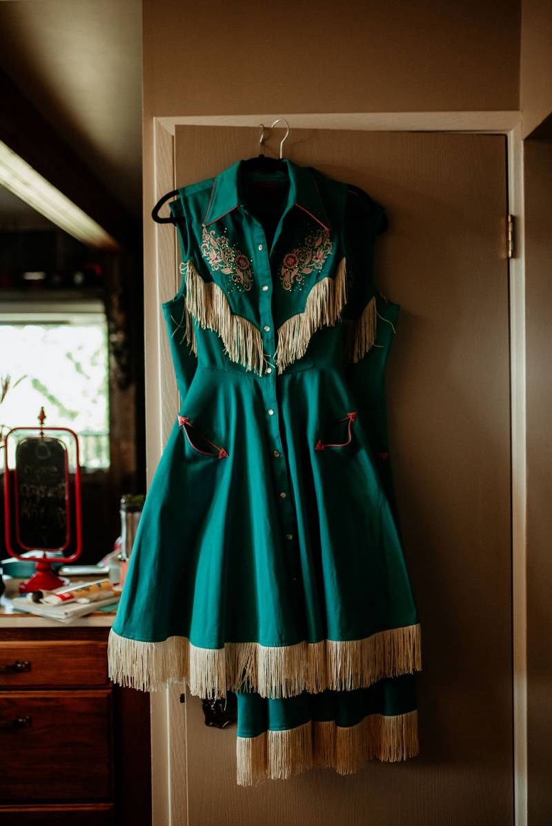 White and teal wedding dress with macramé accents hanging on doorframe  