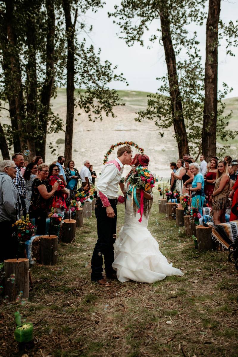 Bride and groom kiss in the middle of the aisle holding multicolored bouquet guests turned to watch 