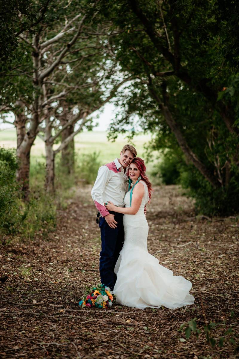 Bride and groom embrace leaning on each other bouquet at feet on forest pathway 