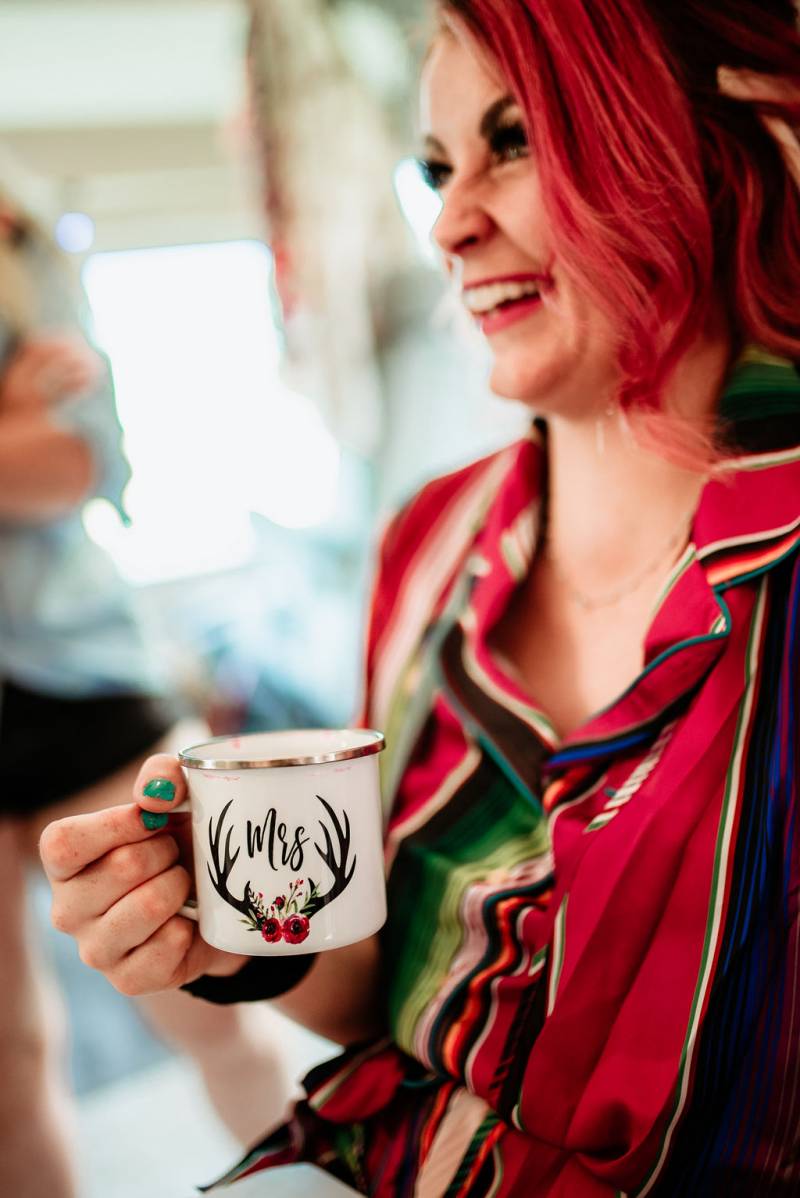 Bride holds white mug in bright red and green shirt smiling 