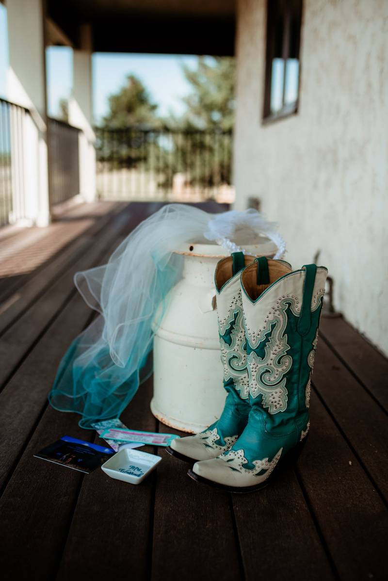 Teal cowgirl boots and white and teal veil on wooden deck 