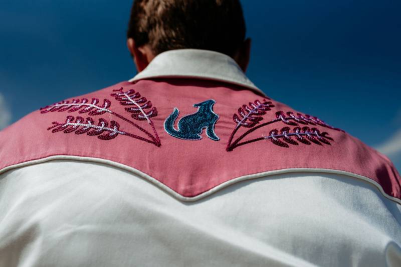 Groom facing away wearing pink and white dress shirt with embroidered details 