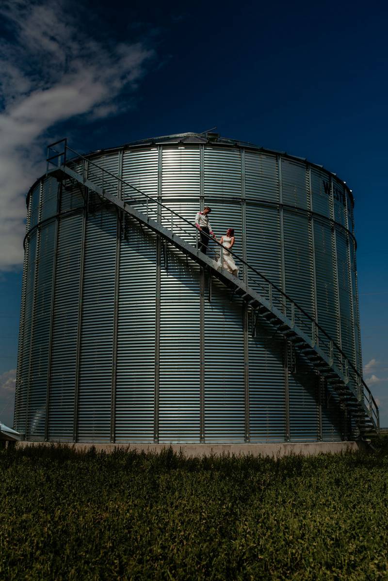 Bride and groom stand on stairway halfway up metal corn silo 