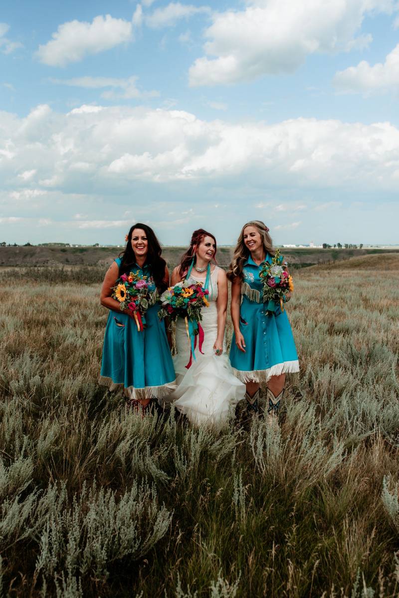 Bridesmaids walk on opposite side of bride holding bouquets in grassy field  