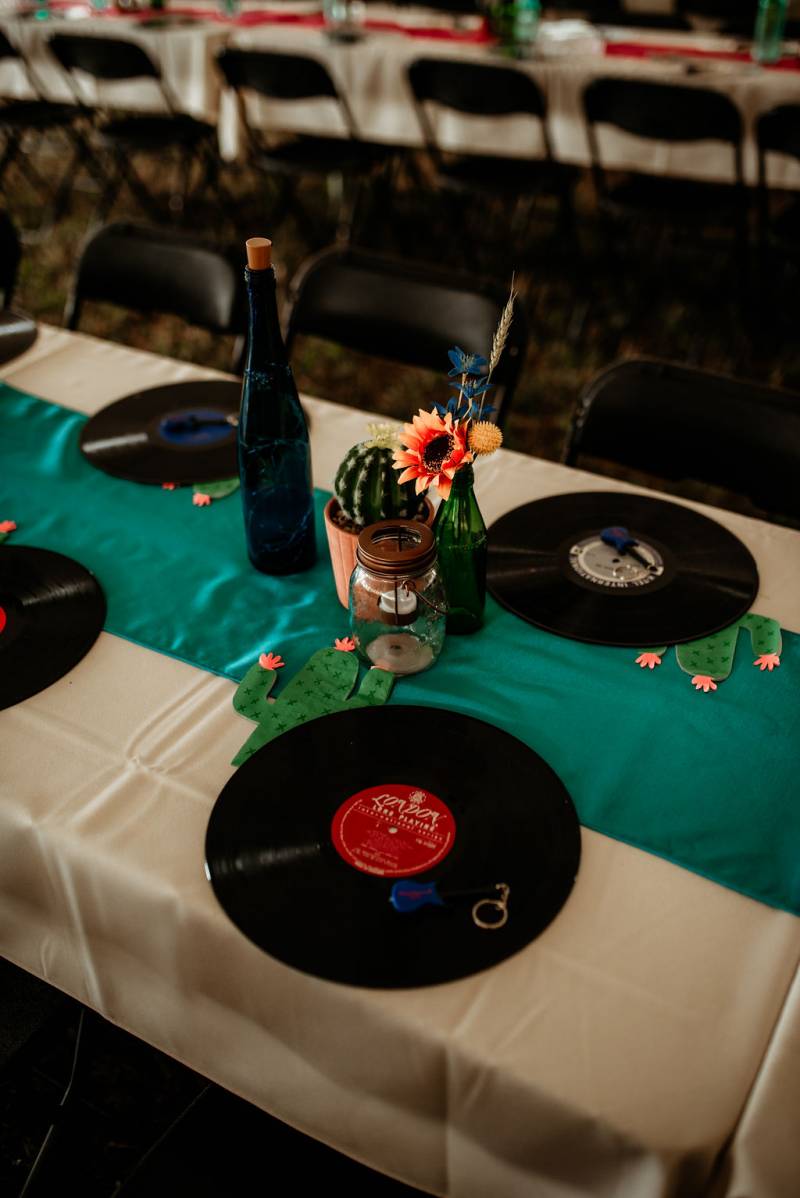 Place settings with records in place of placemats and teal table runner and cactus centerpiece 