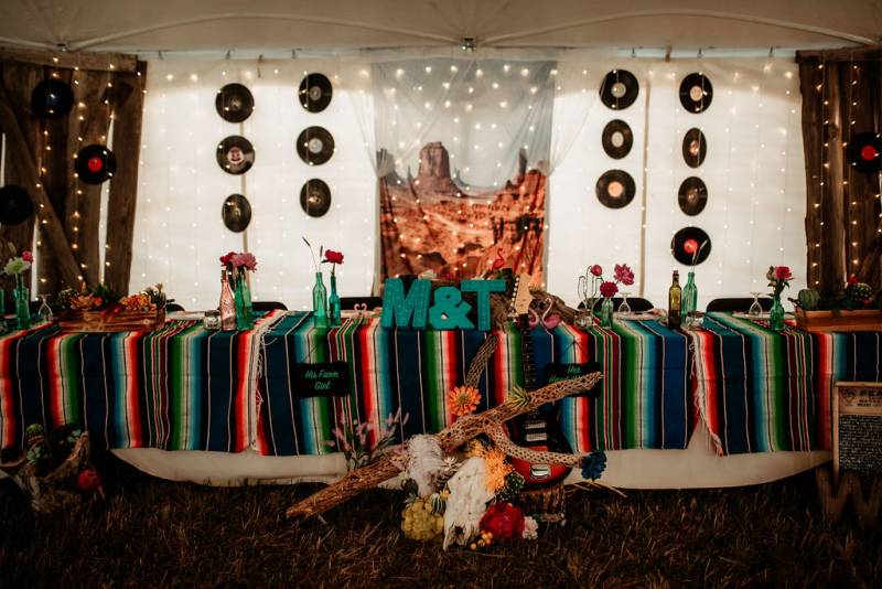 Hanging records on white tent walls behind table with multicolored rug on top and crimson and yellow floral arrangements 