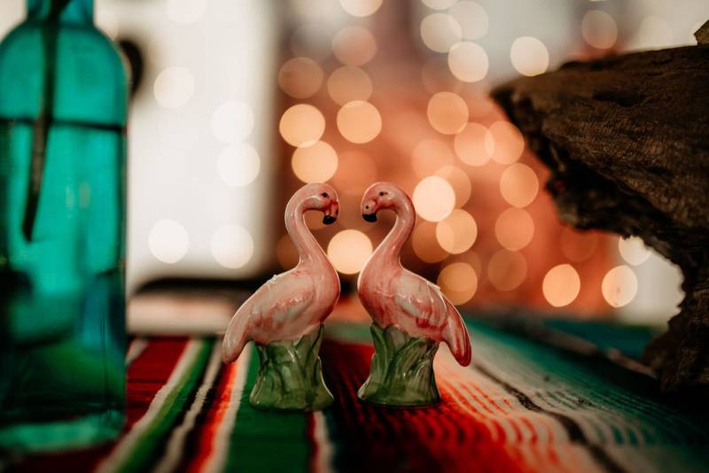 Small flamingo figurines sitting on multicolored tablecloth beside teal bottle 