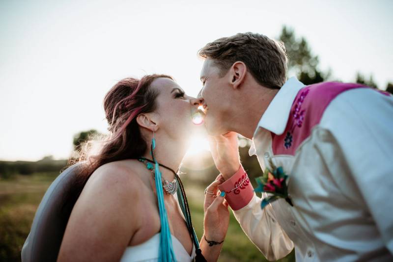 Bride and groom wince while smiling nearly kissing at sunset