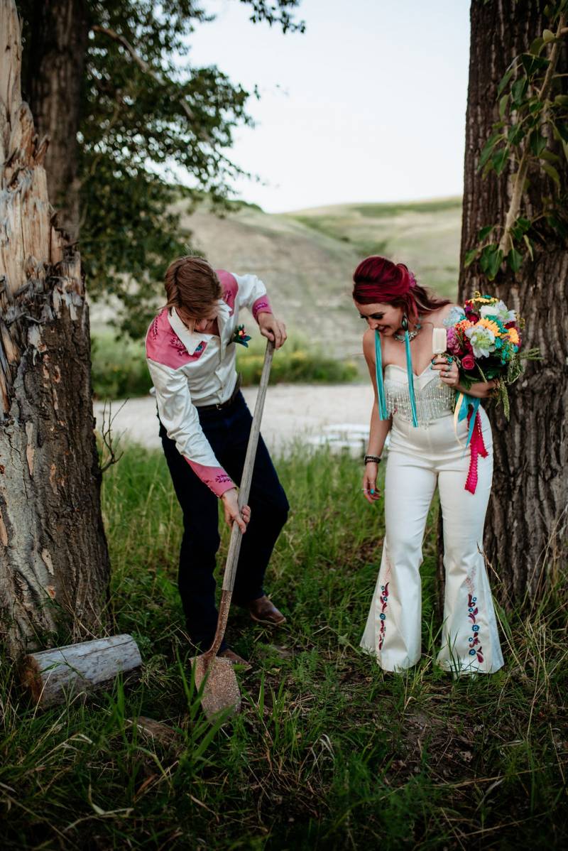 Groom digs with shovel while bride stands to side backing river 