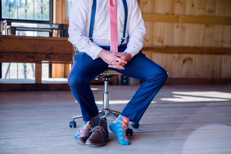 Groom sits on stool shoes off feet showing blue multicolor socks