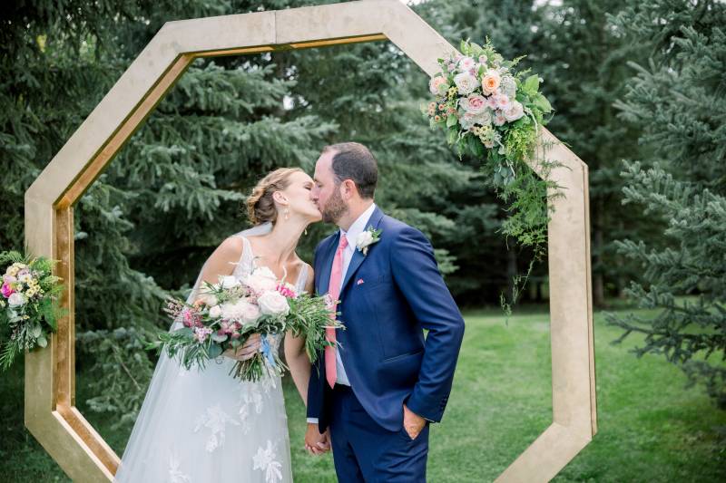Bride and groom kiss in front of gold geometric wedding arch 