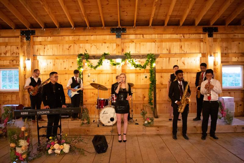Band playing music in large wooden barn in front of wedding arch