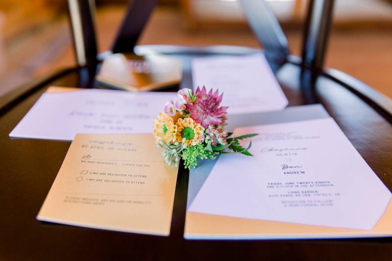 Wedding invitations and pink and yellow boutonniere on wood table 