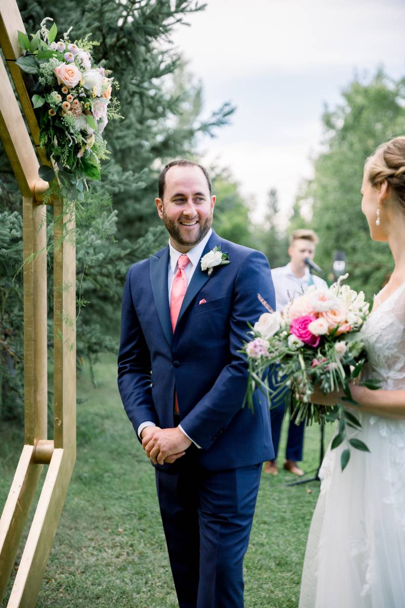 Bride and groom stand facing wedding arch smiling 