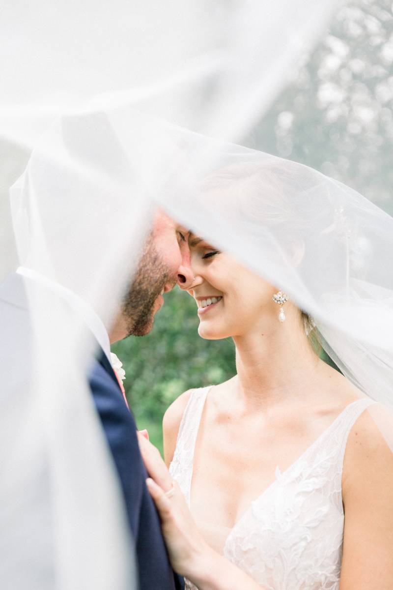 Bride and groom smile under floating white veil 