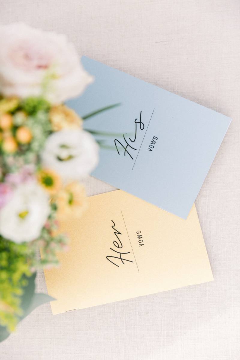 Blue and yellow his and hers vow book beside bouquet 