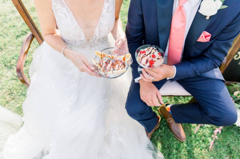 Bride and groom sit on wooden bench holding banana splits 