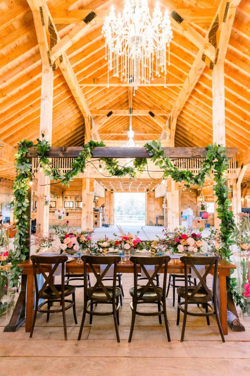 Wedding arch over dark wood table with hanging greenery in barn 