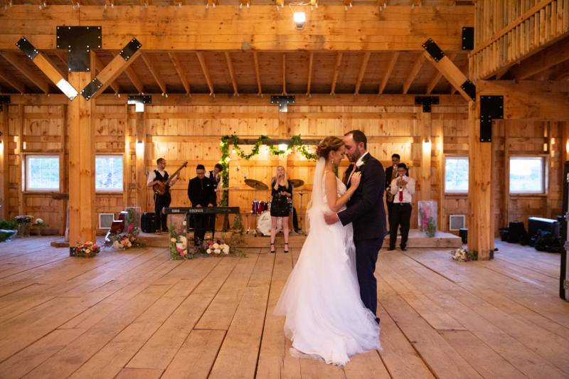 Bride and groom dance on wooden floor touching foreheads in front of band 