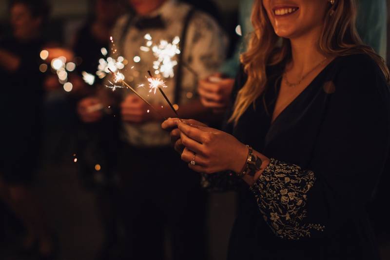 Woman holding sparklers in dark room behind others with sparklers 