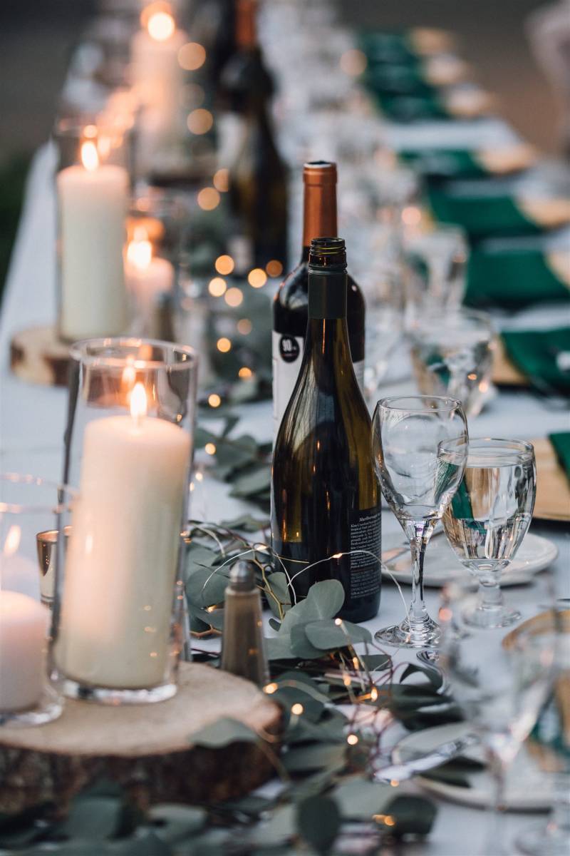 Candle lit table of place setting with green table runner and bottles of wine