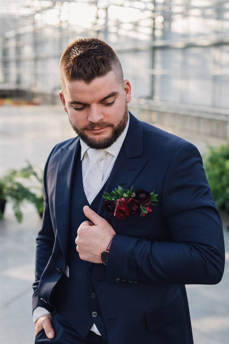 Man in dark blue suit and burgundy boutonniere with hand in pocket 