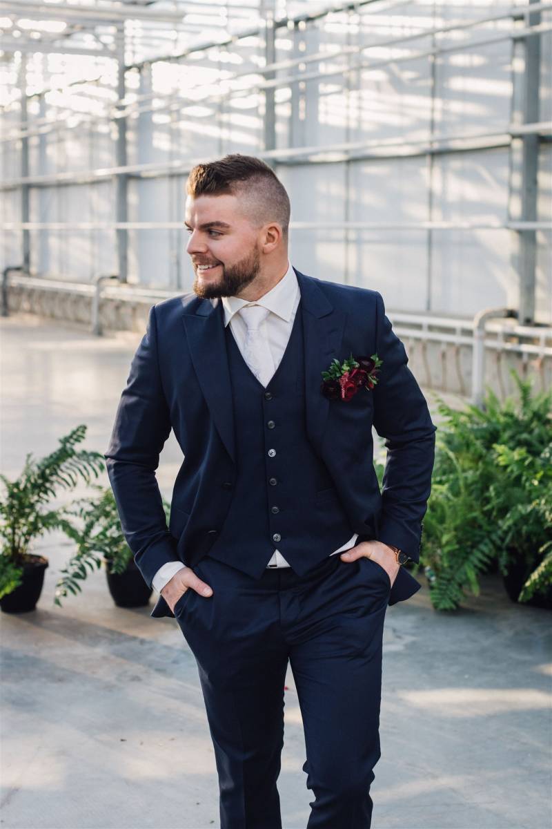 Man in dark blue suit and burgundy boutonniere looks off to side 