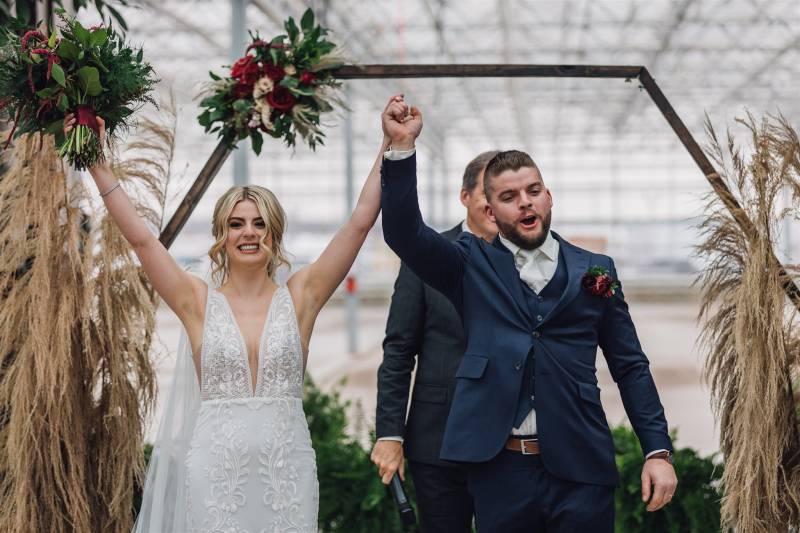 Man and woman hold hands above their heads in celebration in front of geometric wedding arch
