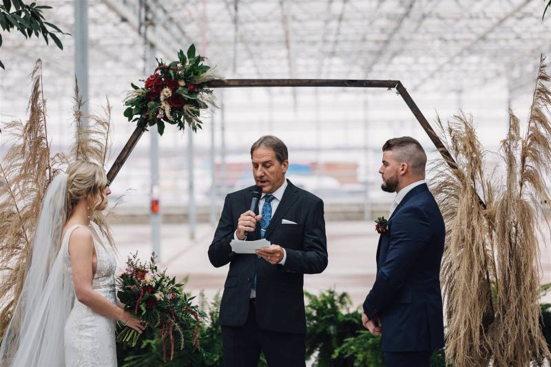 Man and woman stand in front of geometric wedding arch and officiant 