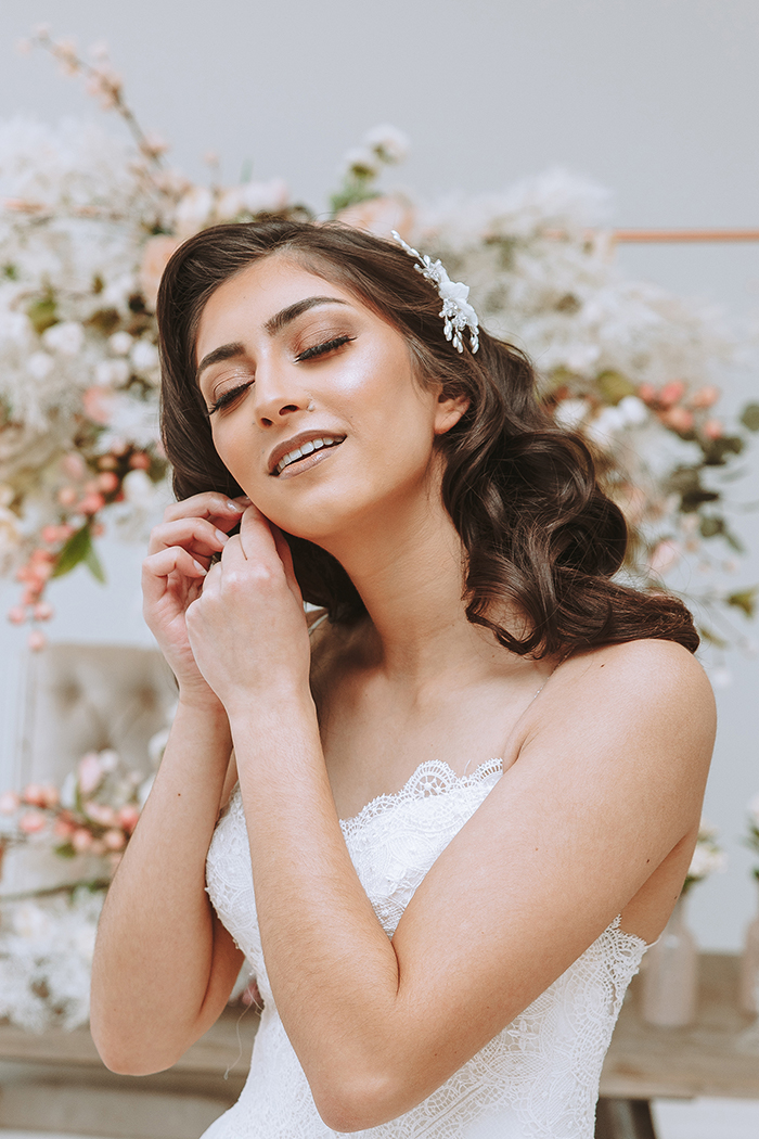 Woman in white dress applies earring eyes closed 