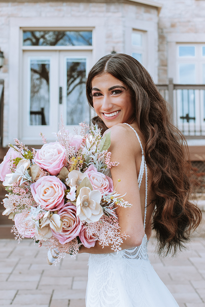 Woman in white dress and long curly brown hair holding blush and pink bouquet 