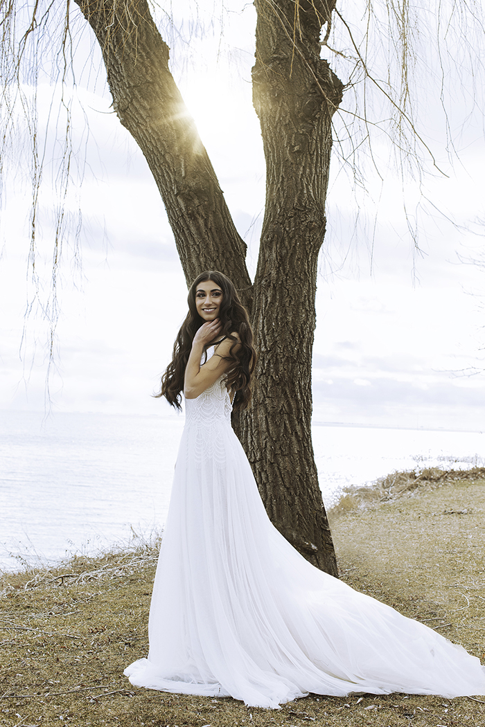 Woman in white dress stands in grassy field in front of tree 