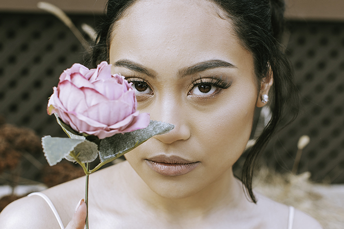 Woman with black hair holds pink flower in front of face