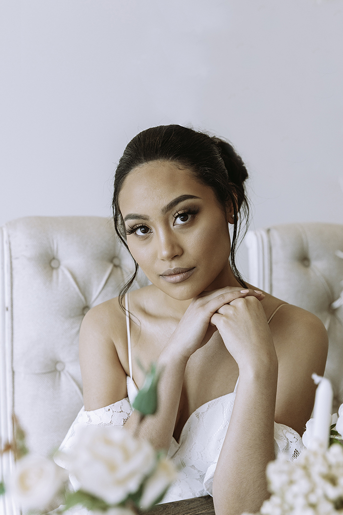 Woman in white shoulder less dress sits arms in front 