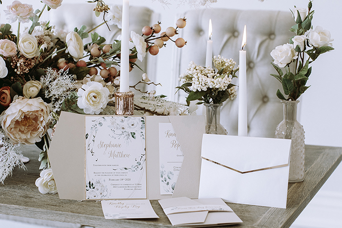 Wedding invitations in blush envelopes sitting on table with large centerpiece and candlesticks