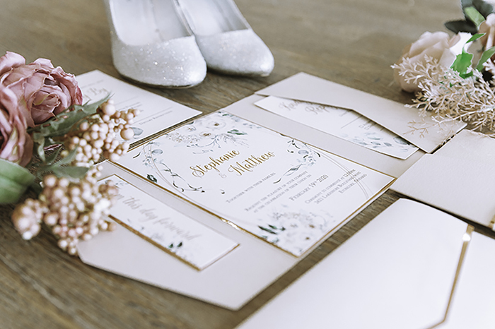 Wedding invitations flat lay with sparkling white heels in background 