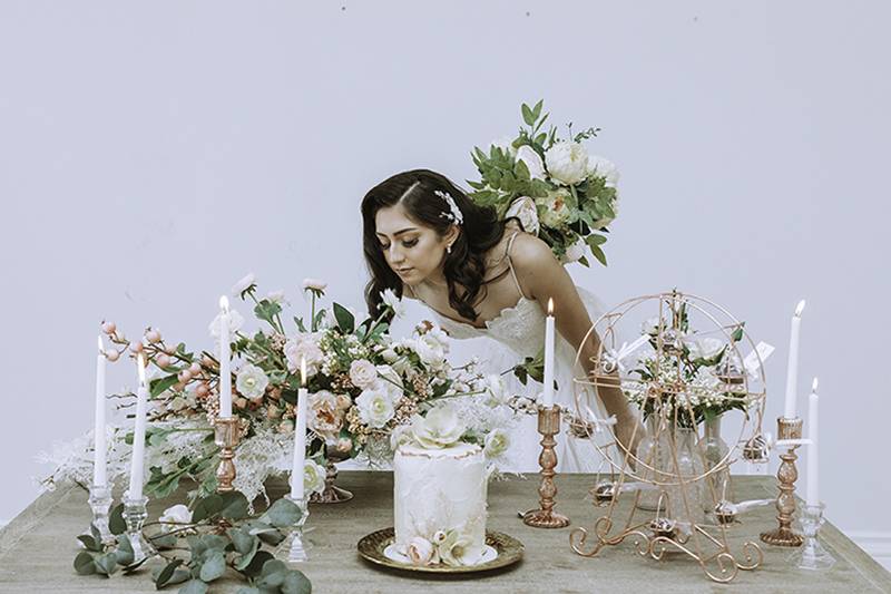 Woman in white dress leaning over cake and floral centerpiece 