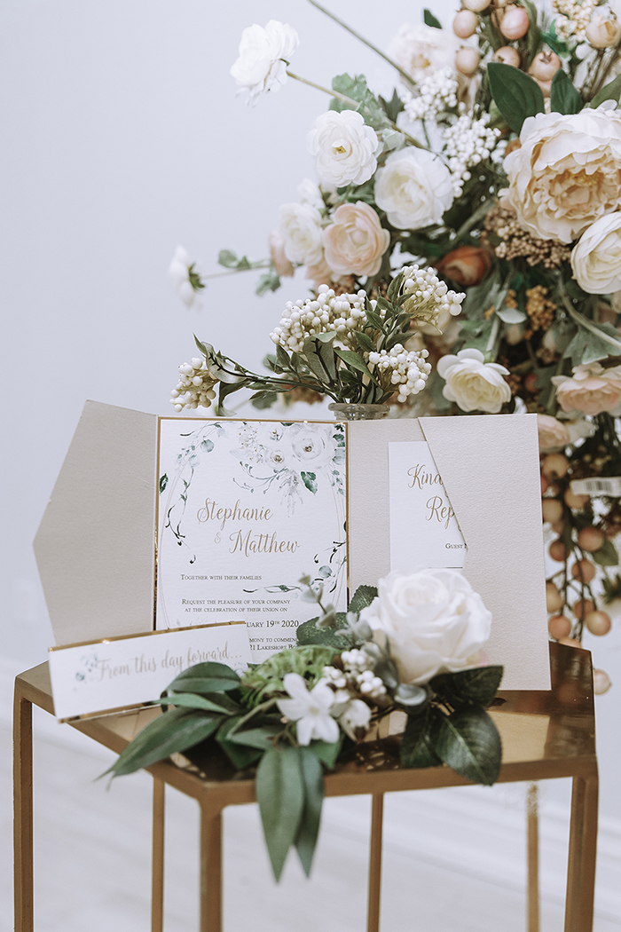 Wedding invitation on top of shiny bronze table and white flowers 