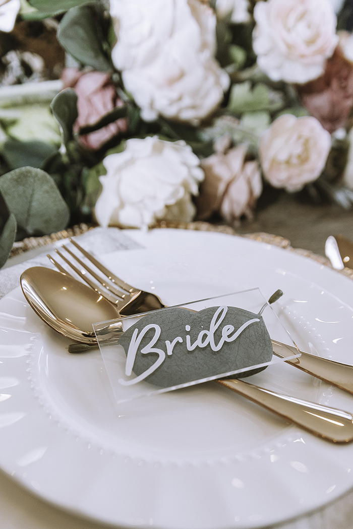 Clear glass Bride tag on top of blush gold cutlery on plate 