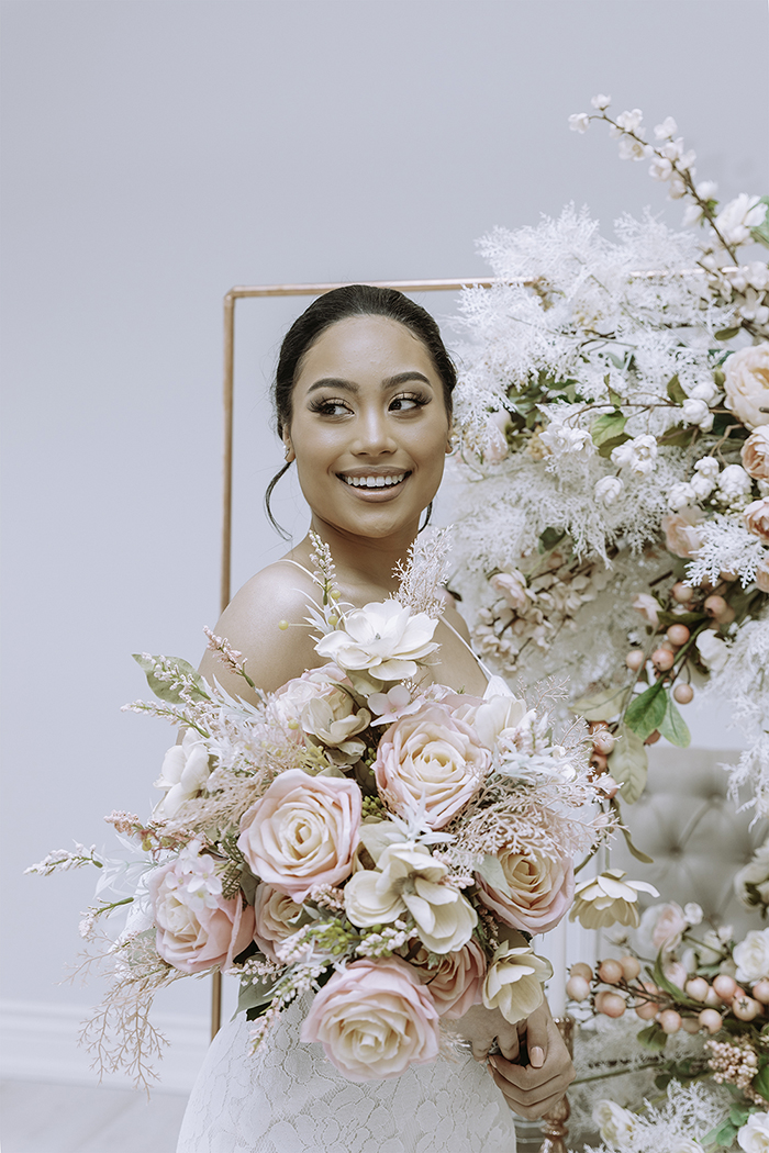 Woman holding blush and white bouquet smiling in white dress 