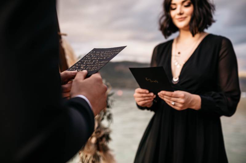 Smiling woman in black dress holding black card facing man in suit holding card