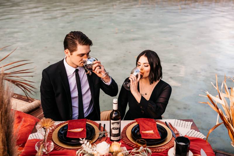 Man and woman drinking from glass sitting at table backing lake 