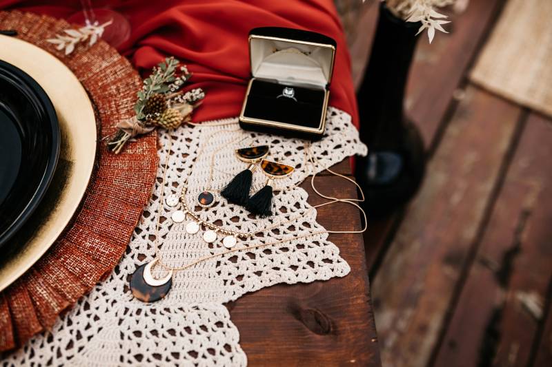 Engagement ring and dark brown jewelry flat lay on wood table with knitted placemats