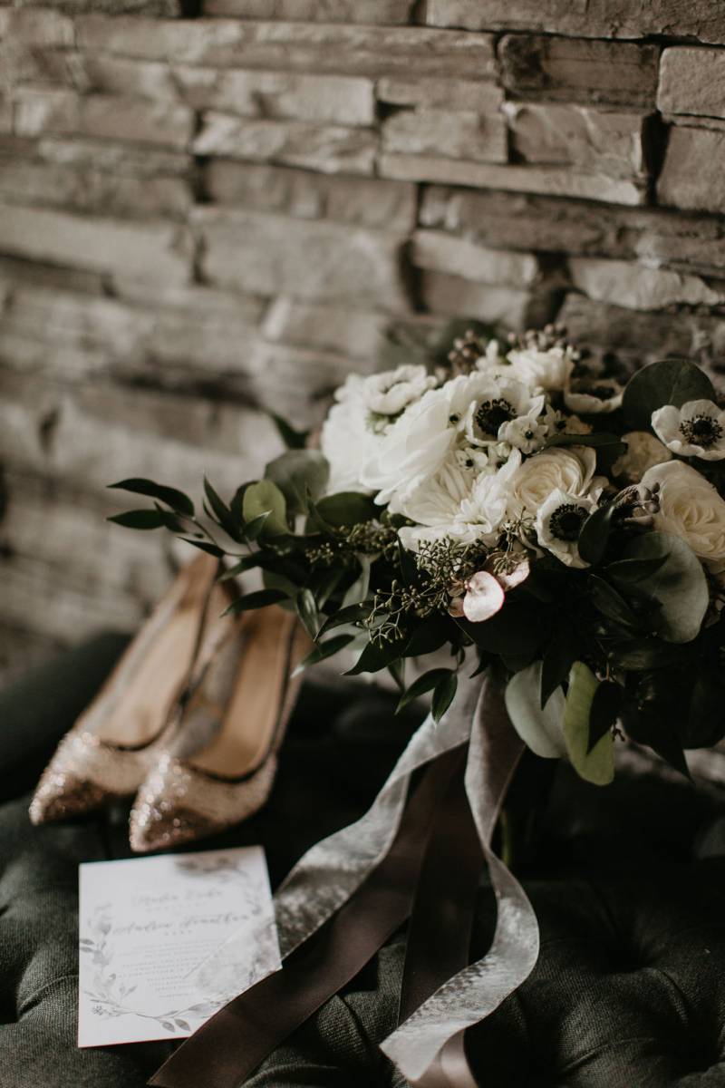 White floral arrangement with white ribbon beside white heels and wedding invitation 
