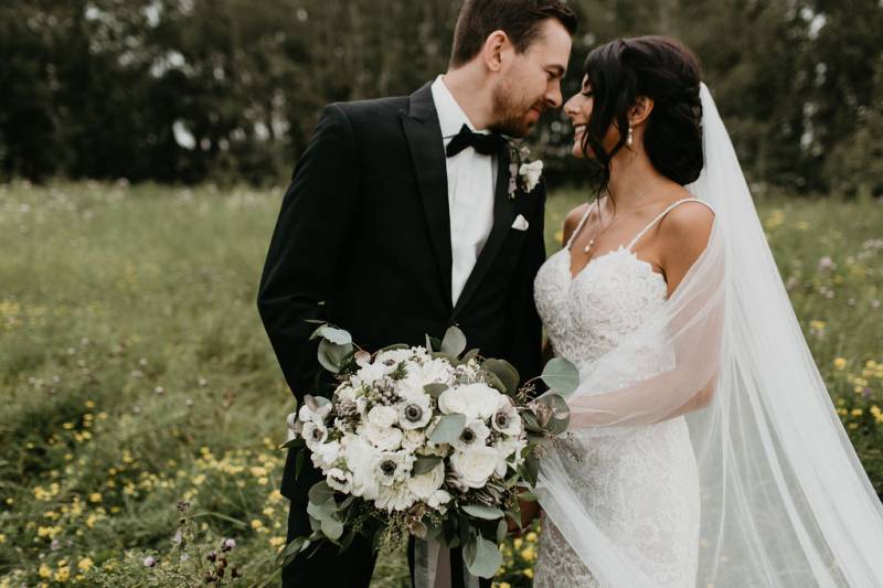 Bride and groom smile holding white bouquet in green dandelion field