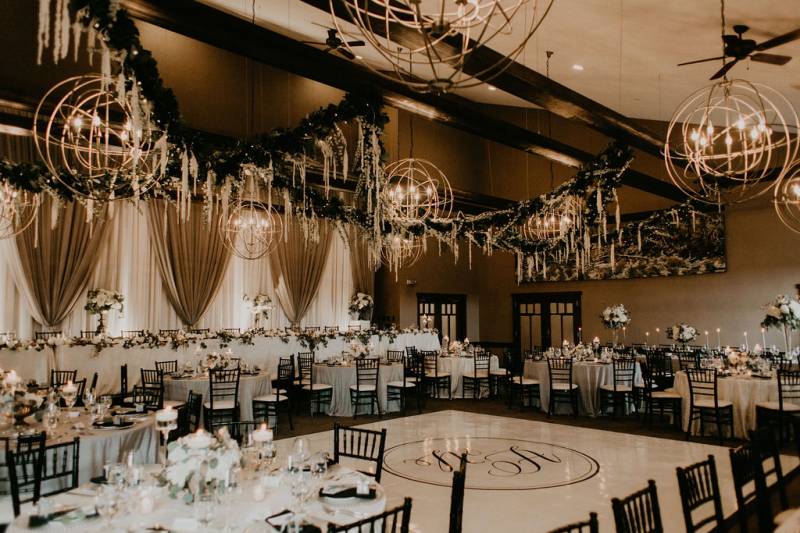 Tables set up around room underneath large round chandeliers and draping fabrics  