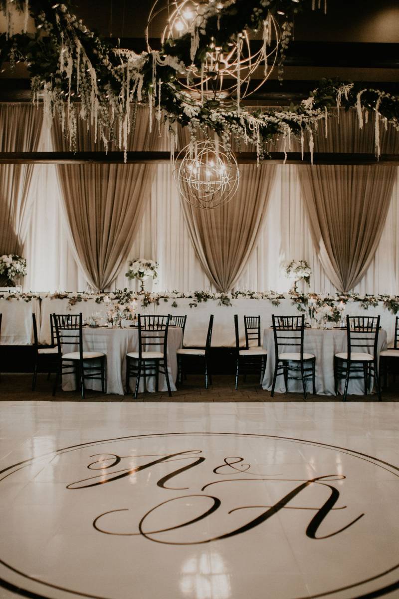 Tables set up around room underneath large round chandeliers and draping fabrics  