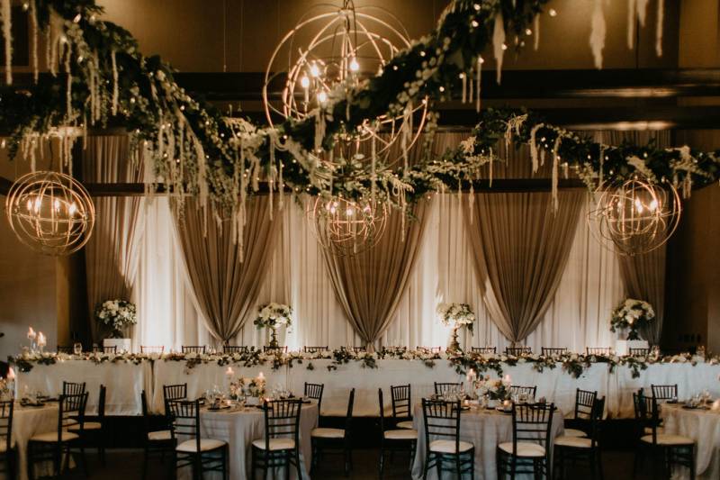 Tables set up around room underneath large round chandeliers and draping fabrics  